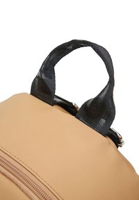 Mochila marrón con un acabado liso y mate. Presenta un asa de tela negra y un zipper con acentos en cobre.