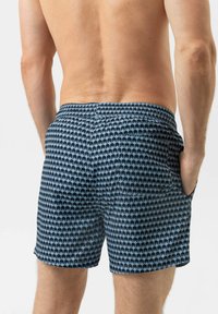 Shorts de bain bleus avec un motif répétitif de palmiers, taille élastique et poches latérales, vus de dos. Texture lisse.