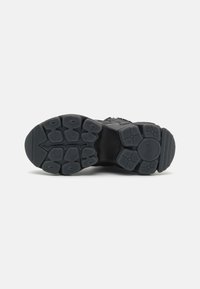 Baskets noires avec une semelle en caoutchouc texturé, arborant une semelle extérieure à motifs multiples pour une meilleure adhérence et une zone de orteil renforcée. Couleur uniforme sur l'ensemble du modèle.