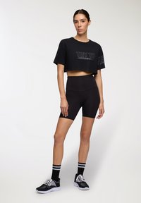 T-shirt nera corta con la scritta "TRY TO" sul davanti, abbinata a pantaloni sportivi neri a vita alta e scarpe da ginnastica nere con suola bianca.