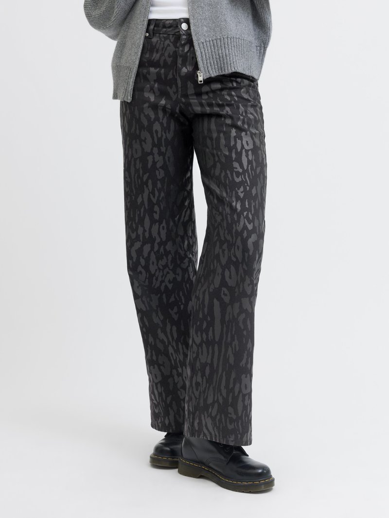 Pantalones de pierna ancha negros con un acabado mate y un sutil patrón de leopardo, combinados con botas negras y un cárdigan gris.