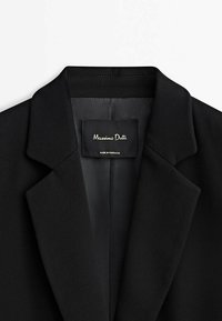 Zwarte blazer met een gelapte kraag, een gladde textuur en twee binnenlabels met "Massimo Dutti" en "Made in Portugal."