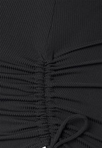 Svart ribbet stoff med innsamlet tekstur og snor detaljer. Har vertikale linjer og en tettsittende design som fremhever materialets strekk.