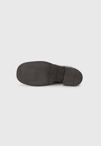 Semelle d'une chaussure de costume en cuir noir avec un avant et un talon en caoutchouc lisse, des coutures visibles et un talon légèrement surélevé.