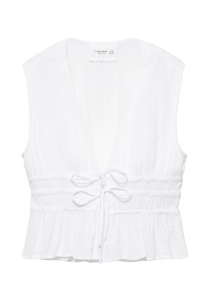 Blouse blanche sans manches avec un profond col en V, taille froncée, deux nœuds à nouer à l'avant et ourlet à volants.