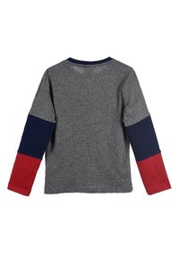 Graues langärmeliges T-Shirt mit Rundhalsausschnitt; hat auf einer Seite marineblaue Ärmel und auf der anderen Seite rote Ärmel. Aus weichem Baumwollmaterial.