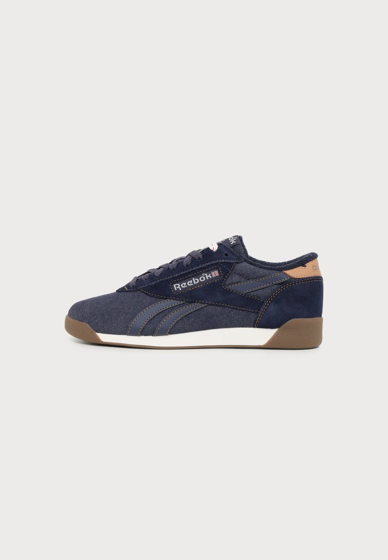 Σκούρο μπλε αθλητικό παπούτσι Reebok με καφέ σόλα και τονισμένο τακούνι, λευκή ενδιάμεση σόλα και λογότυπο στο πλάι και στη γλώσσα, εμφανιζόμενο από την εξωτερική πλευρά.