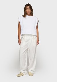 Sudadera blanca texturizada con escote redondo y mangas cortas, combinada con pantalones anchos color marfil y zapatos tipo slip-on en beige claro.