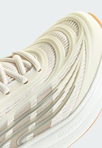 White athletic shoe featuring textured fabric upper with wavy overlay, tonal accents, and rubber sole with visible branding.