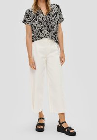 Camisa de manga corta con estampado paisley en blanco y negro, combinada con jeans de pierna ancha de cintura alta en blanco y sandalias de plataforma negras.
