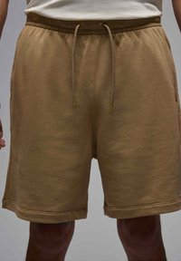 Pantaloni corti di cotone marroni con vita elastica e coulisse, dotati di tasche laterali e vestibilità rilassata. Texture liscia con orli cuciti.