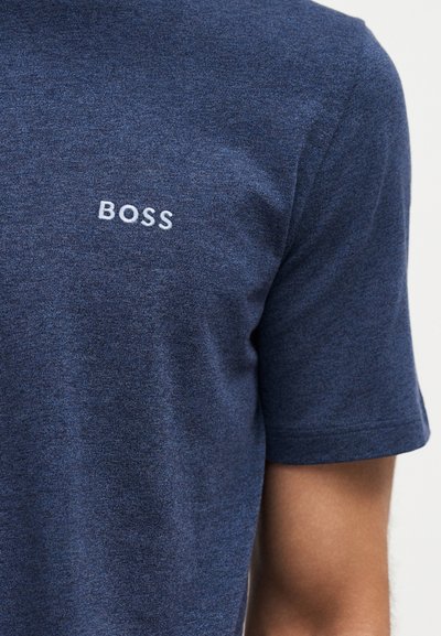 Chemise bleu marine à manches courtes avec inscription blanche « BOSS » brodée sur la partie supérieure de la poitrine, portée par une personne au teint moyen.