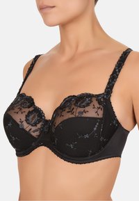 Reggiseno nero con coppe in rete ricamata, motivi floreali, bordi ondulati e spalline regolabili. Presenta un sottobanda liscio e hardware dettagliati.