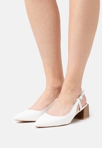 Escarpins blancs à talon slingback avec un bout pointu, fabriqués en matériau lisse. Comprend un talon carré avec une texture en bois et une bride ajustable à la cheville.