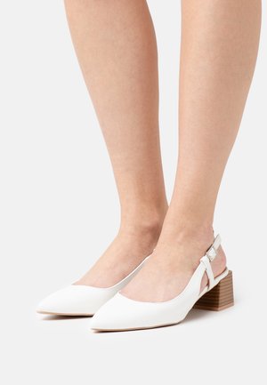 Vita slingback-klackar med spetsig tå, tillverkade av mjukt material. Har en blockklack med trästruktur och en justerbar ankelsnörning.