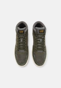 Korkeat tennarit tummanvihreinä ja harmaana, joissa on nahkainen päällinen, pehmustettu nilkkareuna, rei'itetty kärki ja kontrastoiva valkoinen kumipohja.