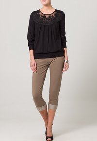Svart långärmad blus med spetsdetalj vid halsen, ihop med beige capribyxor, uppvikta ärmar och svarta högklackade skor.