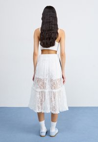 White lace midi skirt with layered ruffles and semi-sheer design. Worn with white socks and light blue shoes. Simple waist construction.