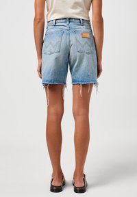 Shorts in denim azzurro chiaro con orlo sfrangiato, vita alta, design a cinque tasche e una patente in pelle marrone sulla parte posteriore della vita.