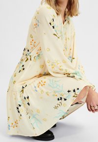 Midi šaty s květinovou výšivkou v jemné krémové látce, s dlouhými rukávy, volným střihem a černými kotníkovými botami.