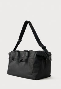 Μαύρη τσάντα duffel από υφαντό νάιλον, με διπλές λαβές στην κορυφή, ρυθμιζόμενο ιμάντα ώμου και ανάγλυφο λογότυπο στο μπροστινό μέρος.