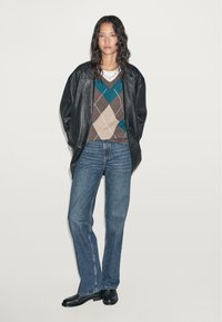 Zwarte leren oversized jas, gestreepte bruine, teal en beige trui met V-hals, blauwe recht slim jeans en zwarte enkellaarsjes.