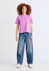 T-shirt rosa a maniche corte con una vestibilità comoda, abbinata a jeans blu a gamba larga e sneakers bianche. Tessuto morbido, stile casual.