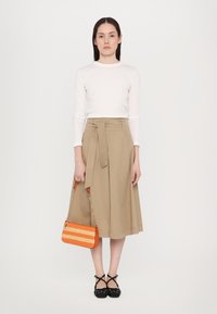 Jupe midi beige avec une ceinture à nouer, assortie à un haut à manches longues blanc. Les accessoires comprennent un sac à main à rayures orange et des chaussures Mary Jane noires.