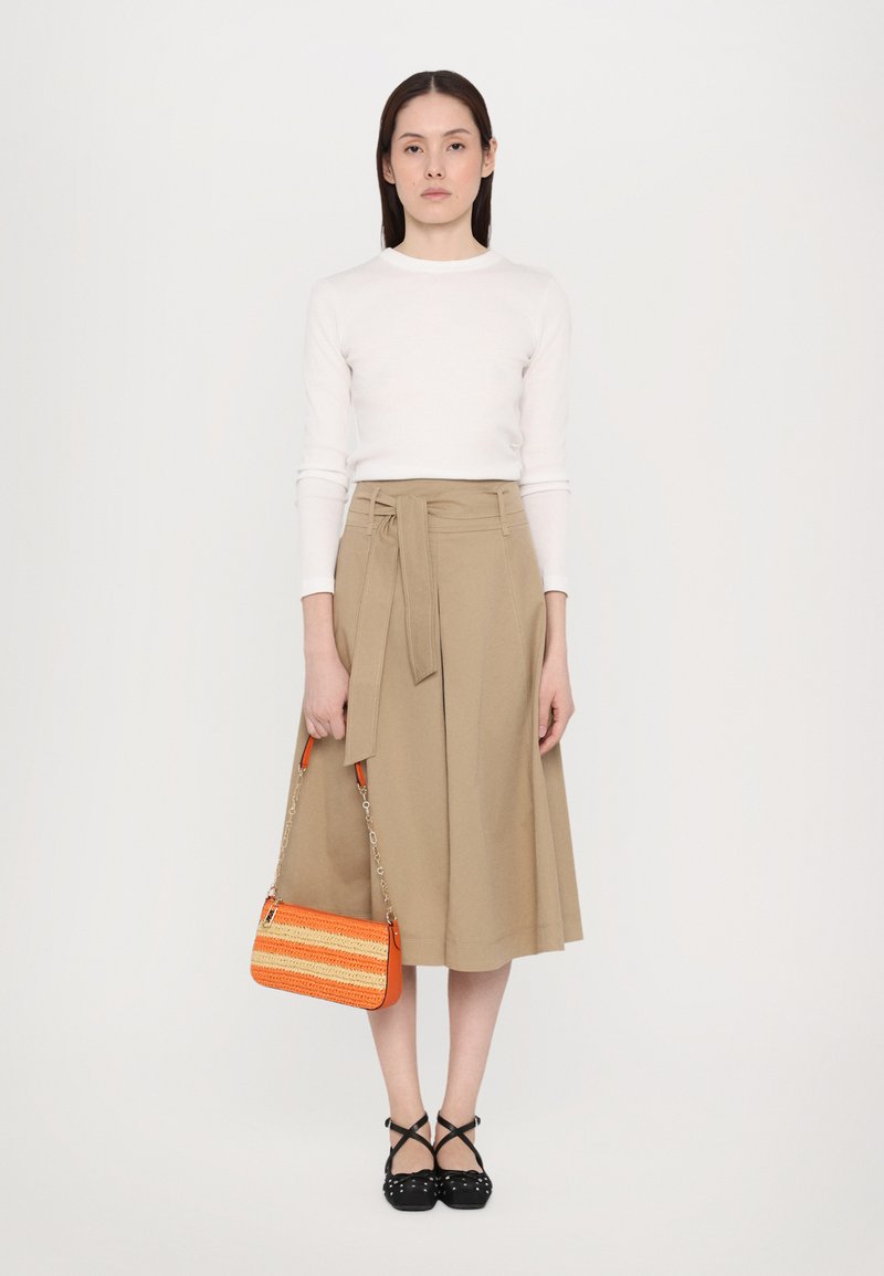Jupe midi beige avec une ceinture à nouer, assortie à un haut à manches longues blanc. Les accessoires comprennent un sac à main à rayures orange et des chaussures Mary Jane noires.
