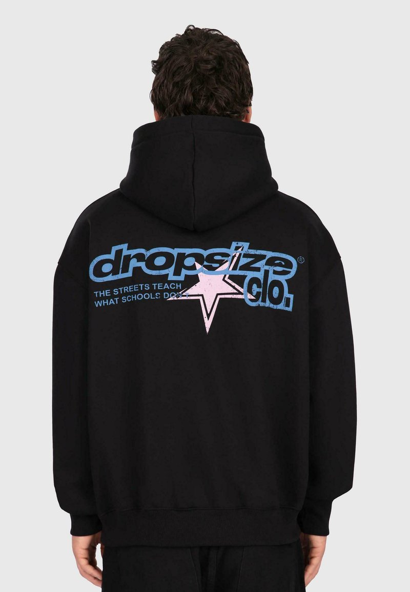 Man wearing black hoodie with large blue and pink "dropsize clo." text and star graphic on the back, standing against a plain background.