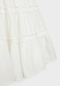 Jupe blanche à plusieurs volants présentant un tissu texturé avec des coutures froncées et des détails froncés. L'ourlet est légèrement évasé pour un volume supplémentaire.