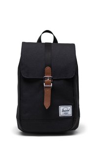 Black fabric backpack with a flap closure, brown leather strap and silver buckle, featuring a logo patch on the front bottom.