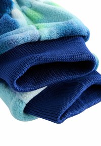 Tissu en polaire aux nuances de bleu et de vert, présentant une surface texturée et lisse. Manches en matériau côte à côte de couleur bleu foncé.