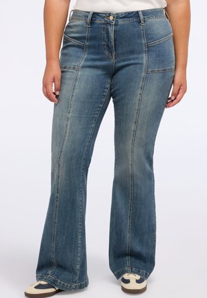 Jean évasé en denim bleu moyen avec des coutures contrastées, comportant des poches avant et une fermeture par bouton. Texture douce avec une coupe classique.