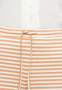 Ριγέ παντελόνια σε απαλό πορτοκαλί και κρεμ, με κορδόνι στη μέση, κατασκευασμένα από ελαφρύ ύφασμα με υφή.