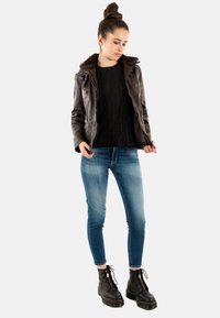 Veste en cuir marron avec col en fausse fourrure, pull texturé noir, jean skinny bleu clair et bottines noires à lacets.