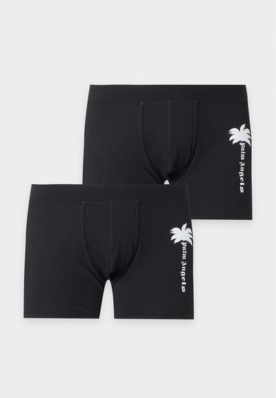 Deux boxers noirs avec un graphisme de palmier blanc et le texte "palm angels" sur la cuisse gauche, présentés sur un fond clair uni.