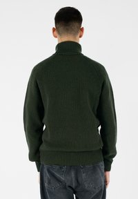 Maglione lavorato a maglia di un verde scuro, caratterizzato da una texture, con un collo alto e polsini a coste. Presenta maniche raglan e un'ampia vita per una vestibilità aderente.