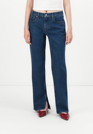 Donkerblauwe denim jeans met een rechte snit, voorzien van zijzakken, een knopenfly en subtiele stikdetails; gecombineerd met rode schoenen.