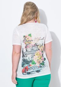 Camiseta de algodón blanca con un llamativo estampado de flores y paisaje urbano en la parte posterior, con el texto "Hermosa Fantasía" escrito de forma prominente.