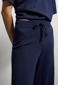 Close-up van een persoon die marineblauwe gebreide broek draagt met een geribbelde elastische tailleband en een gestrikt trekkoord.