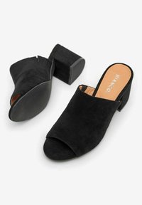 Black suede open-toe mules with a chunky heel. The design features a smooth texture and a flat black rubber sole for grip.