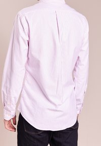 Ljusrosa och vit randig långärmad skjorta med böjd nederkant, knappmanchetter och en bakfåll för extra designdetalj.