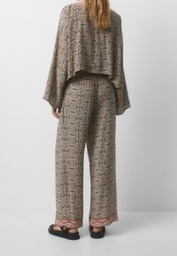 Ensemble deux pièces à motifs comprenant un haut ample et court ainsi qu'un pantalon à jambes larges. Confectionné dans un tissu doux avec des motifs géométriques en beige, noir et touches de rouge.