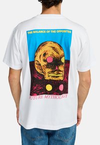 White cotton t-shirt featuring a colorful graphic of a skull-like face, with blue, pink, yellow, and black accents, and text at the bottom.