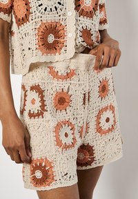 Set in uncinetto composto da un top a maniche corte e pantaloni corti, realizzato con filato crema decorato con motivi floreali arancioni e marroni e una finitura testurizzata.