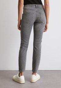 Jean en denim gris avec une coupe ajustée, cinq poches, une taille mi-haute et une texture lisse, associés à des baskets blanches.