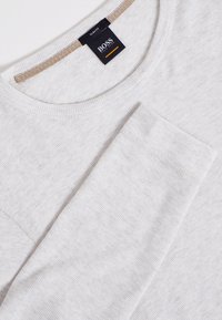 Ljusgrå långärmad tröja med texturerad yta och slim fit. Har en rund halsringning och en kontrasterande brun detalj vid kragen.