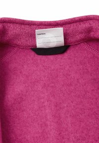 Wnętrze różowej bluzy z teksturowanego materiału. Prążkowany dekolt i metka z napisem „Byłem tu:”.