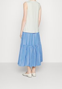 Haut sans manches vert clair associé à une jupe à volants rayée bleu et blanc, avec un ourlet volanté et des chaussures plates blanches.